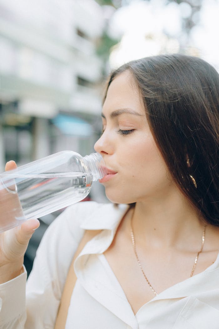 Side view of a young woman drinking water from a bottle in an outdoor setting.